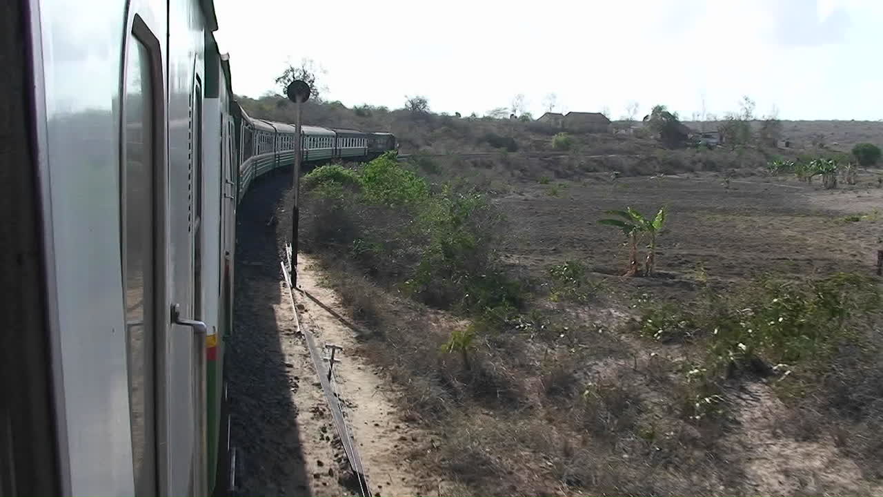 un tren viaja por las vías pasando por pequeños edificios, chozas y personas de pie al lado