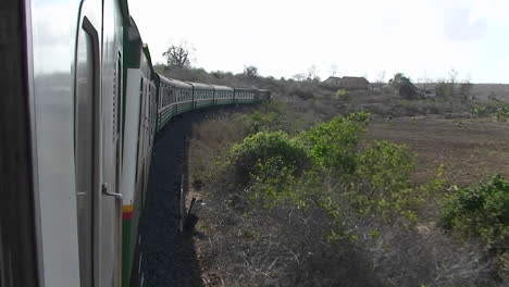 un tren viaja por las vías pasando por pequeños edificios, chozas y personas de pie al lado