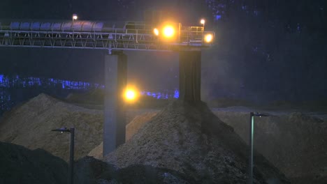 a nighttime look at a conveyor belt system transporting wood shavings into a large pile at a plywood production facility