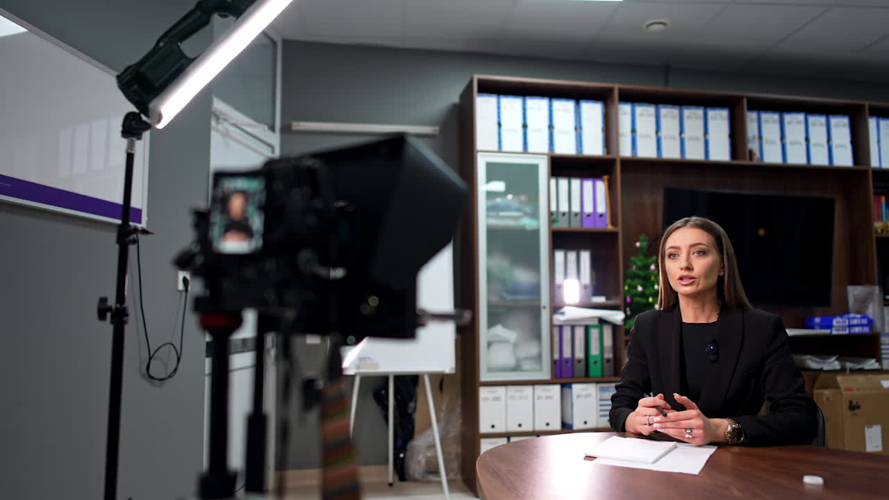 Female speaker sitting in the office at the desk. Good-looking Caucasian blogger creating video content.