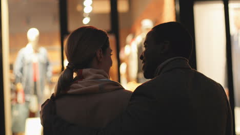 rear view of a couple hugging and talking in front of a shop window on the street at night