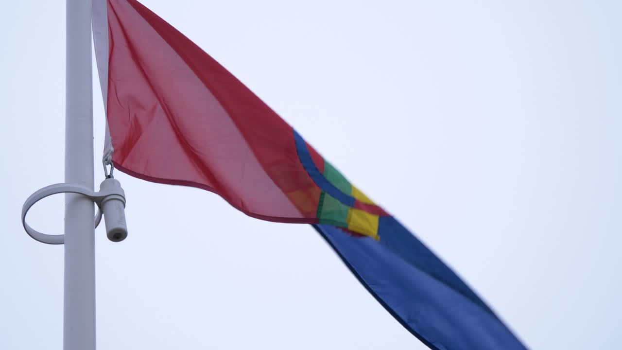 Samisk flag, farverigt flag, der vajer i toppen af en flagstang på en overskyet dag - lav vinkel, tilt op, nærbillede.