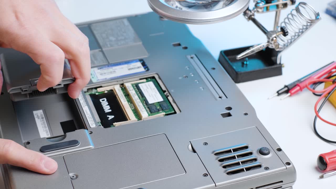 Computer technician removing a battery from a laptop, close up of hands disassembling a computer