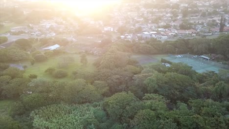 drone-flying-over-tennis-courts-and-abandoned-buildings-above-a-canal-with-roads-and-residential-houses-in-the-distance