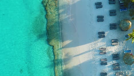 Drone-top-down-rising-above-Grote-Knip-beach-Curacao-above-reclining-beach-chairs,-long-shadows