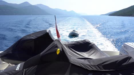 boat with jet ski's under protective cover at aft deck towing rubber boat at sea with green forested mountains