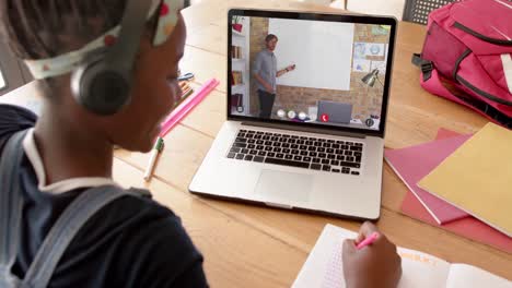 estudiante afroamericana usando una computadora portátil para una lección en línea con un profesor caucásico en la pantalla