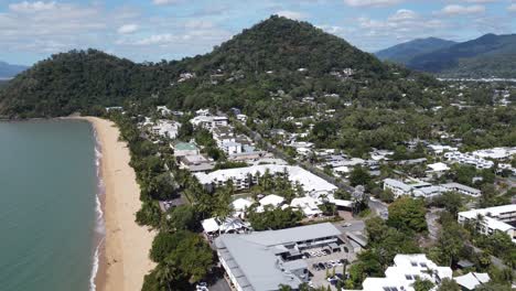 4k aerial view of a tropical sandy beach and beachside small town laced with luxury hotels in north queensland, australia