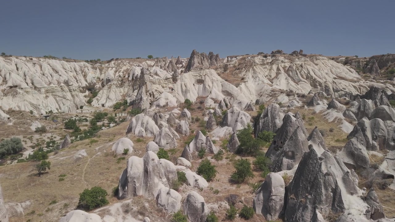 Ripresa aerea con drone in avanzamento 4K 10-bit sopra le tradizionali case rupestri a Goreme, Cappadocia. Filmato panoramico di una soleggiata giornata estiva di antiche abitazioni rupestri e architettura unica sotto cieli sereni