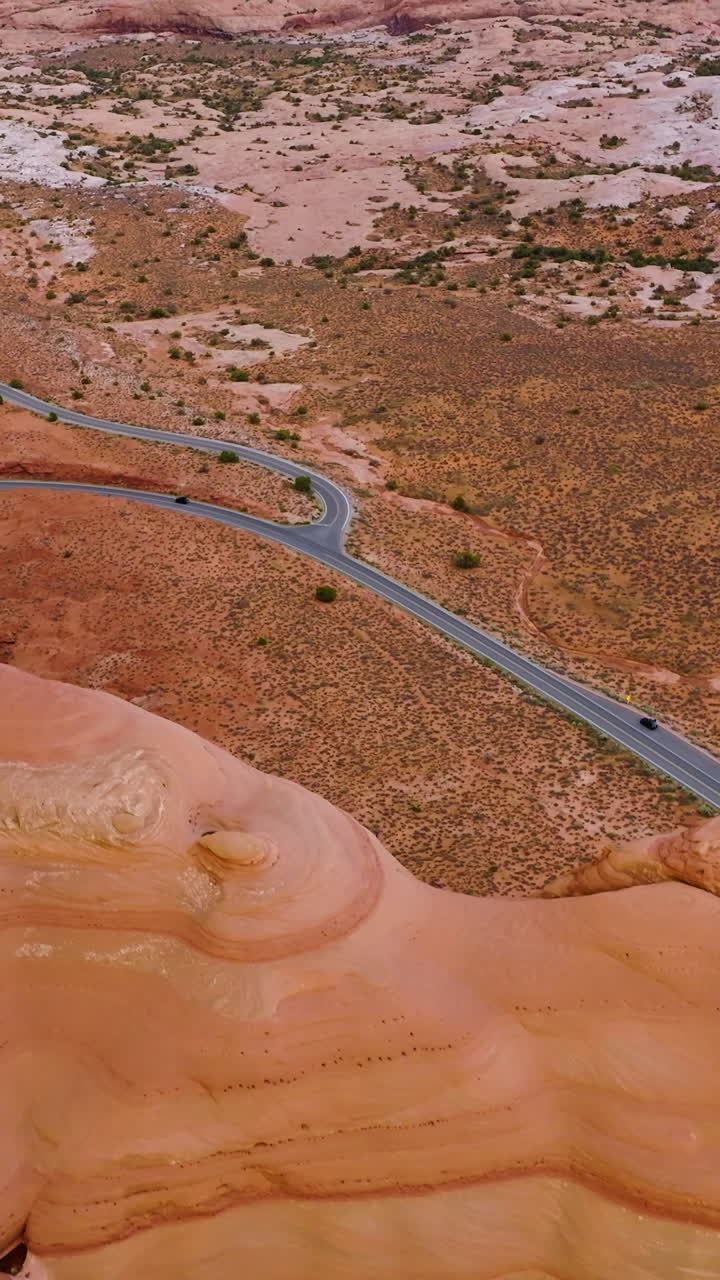 Rounded smooth rocks of canyons in National Arches Park, Utah, USA. Lonely car following the road in the deserted valley. Top view. Vertical video