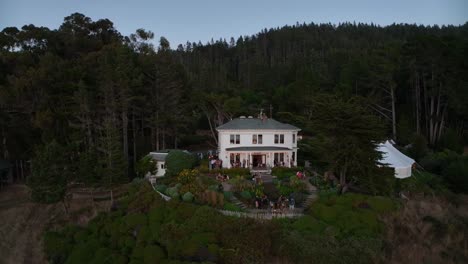 wide drone shot of a private wedding venue in the evening, people mingling outside with drinks