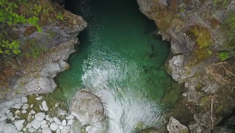 Inclinación-Aérea-Hacia-Arriba-Del-Arroyo-Río-Azul-Que-Corre-Entre-Acantilados-Rocosos-Rodeados-De-Vegetación,-El-Bolsón,-Patagonia-Argentina