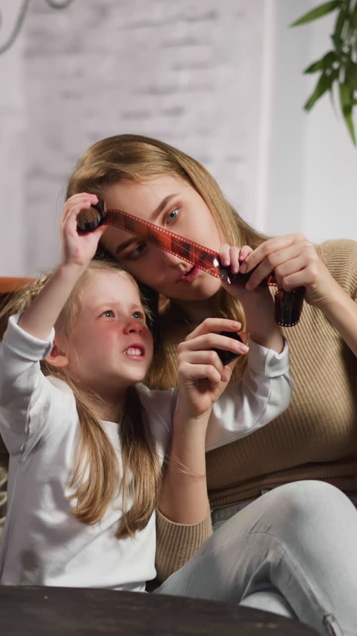 Serious fair haired woman with little daughter and husband points to shot on negative film on couch in stylish living room slow motion