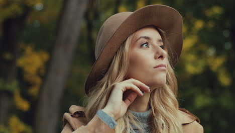 vista de primer plano mujer rubia joven caucásica en un sombrero pensando en algo en el parque en otoño