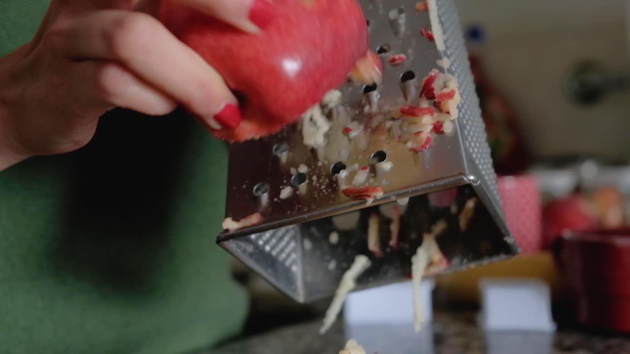 Close up of woman grating a red apple with skin on large holes of box grater