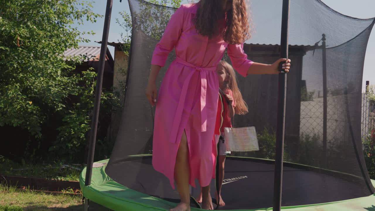Adult Guides Kid Across Trampoline Safely, Woman Helps Young Girl Through Net In Sunny Yard, Mother And Adult Assist Young Children During Trampoline Play In Sunny Backyard Environment