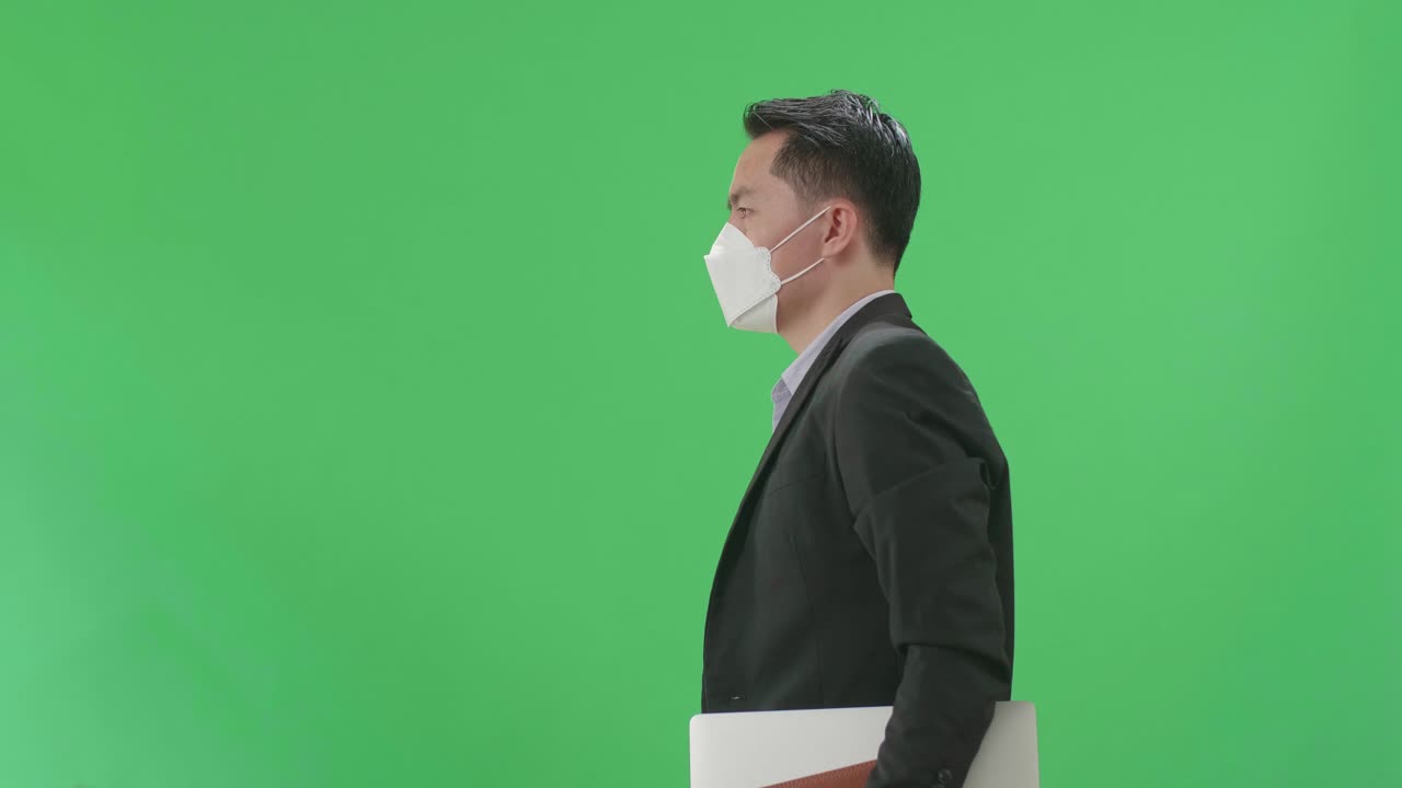Side View Of Asian Business Man Holding Book And Document While Walking On Green Screen Chroma Key, Wear Medical Mask