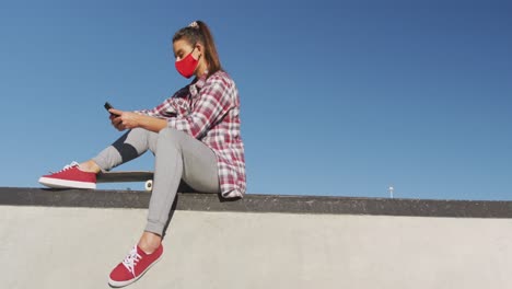 caucasian woman wearing face mask, sitting and using smartphone