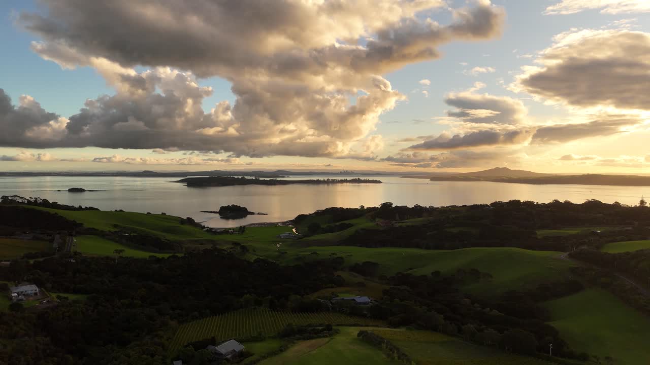 Dramatic sunset sky with clouds reflecting on calm ocean, Waiheke Island shore, New Zealand. Aerial forward