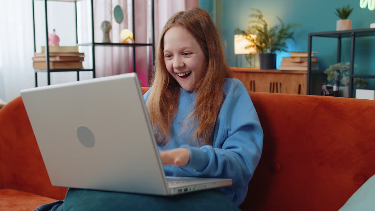 Happy child girl using laptop typing playing game good positive news celebrate online win at home