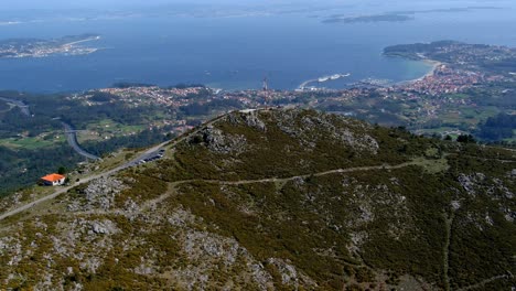 Vista-Aérea-Sobre-El-Paisaje-De-Miradoiro-Da-Curota-Con-Mástil-De-Radio-En-La-Cima-De-Una-Colina-Y-Ria-De-Arousa-En-Segundo-Plano