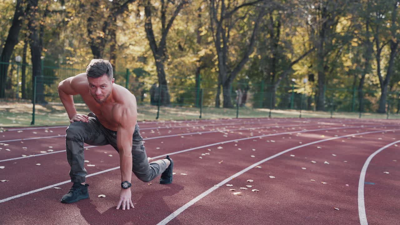 Handsome sportsman doing his workout in the open air. Muscular athlete with sporty body starts running on the outdoor stadium in autumn.
