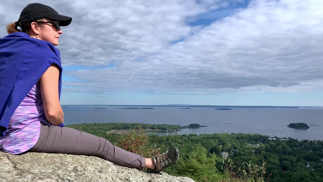 캠든 메인 근처 마운트 배티 꼭대기에서 캠든 메인을 내려다보는 4k 여성