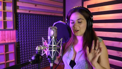 Woman-with-headphones-dancing-and-singing-in-a-studio-on-a-retro-microphone