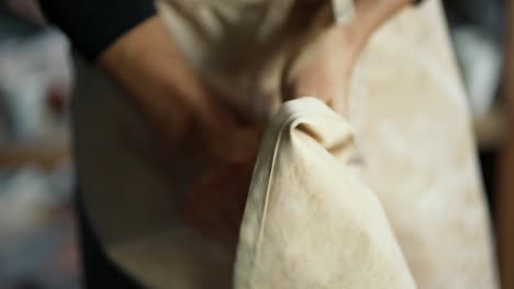 Young-happy-potter-wipes-his-hands-on-his-apron-after-working-with-clay.-Close-up.-The-concept-of-traditional-professions