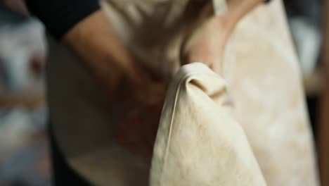 young happy potter wipes his hands on his apron after working with clay. close-up. the concept of traditional professions