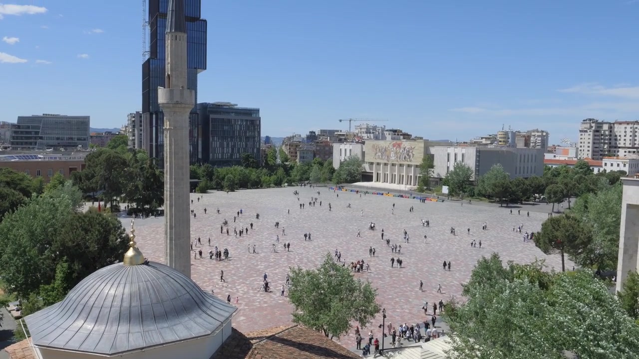Cúpula e minarete da Mesquita Et'hem Bej com vista para a movimentada Praça Skanderbeg, com pessoas atravessando a praça aberta em Tirana, Albânia