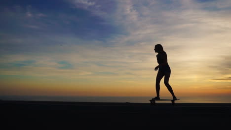 imágenes en cámara lenta capturan a una impresionante joven patinadora en pantalones cortos, montando su tabla en un camino de montaña al atardecer, con las montañas proporcionando una vista panorámica
