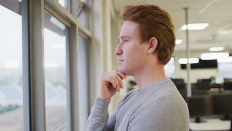 profile of thoughtful caucasian creative businessman touching face and looking through window