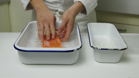 male chef giving fresh salmon fillet salt bath for delicious taste,close up