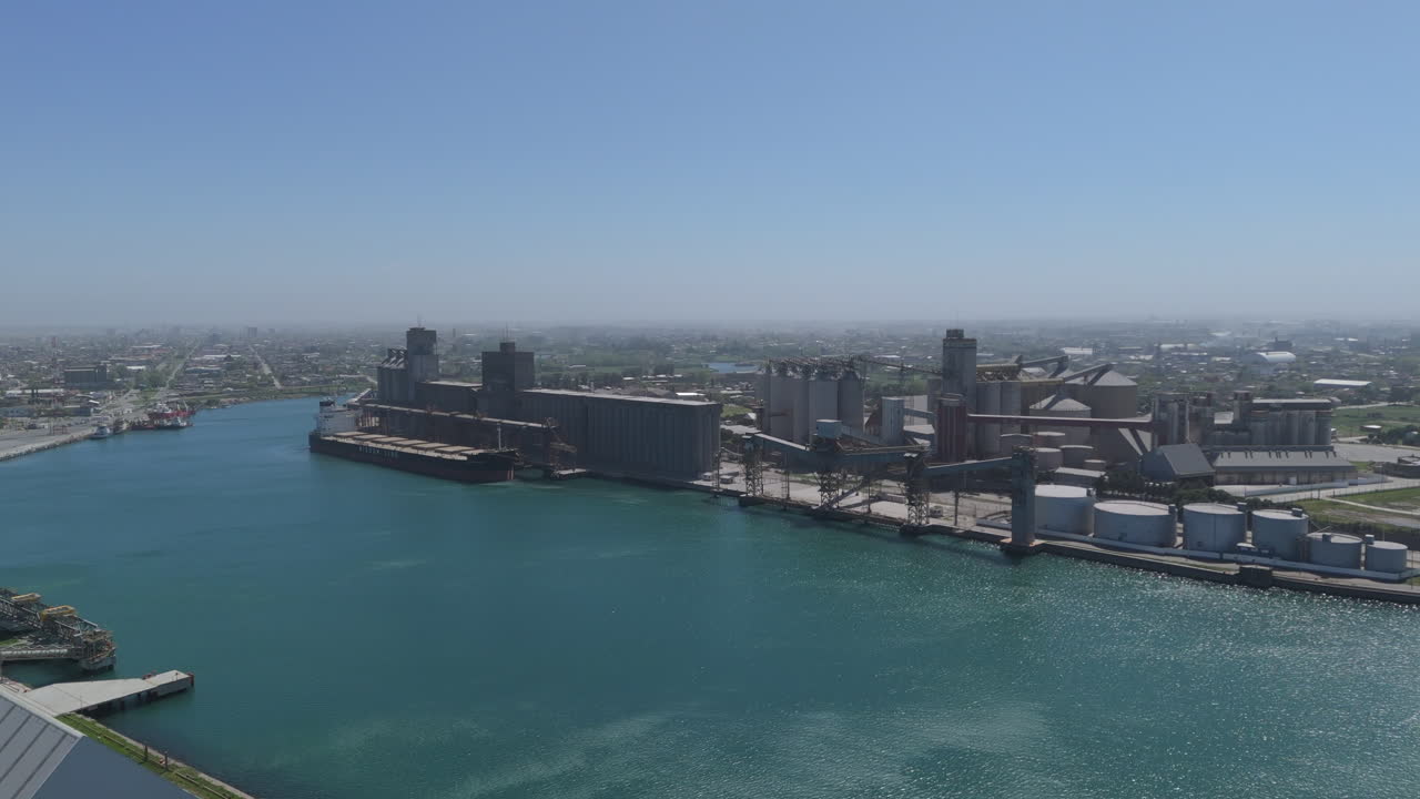 drone de seguimiento hacia adelante disparado sobre el puerto de necochea, argentina. edificios de almacenamiento de contenedores de envío hacen escena, con cielos soleados. disparado 4k-60fps