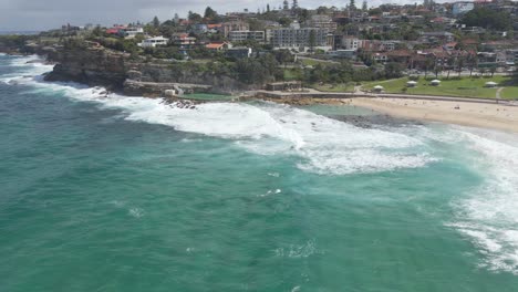 Playa-De-Bronte---Vista-Aérea-De-Las-Olas-Del-Océano-Rompiendo-En-Los-Baños-De-Bronte-Y-En-La-Cuenca-Rocosa-De-Natación-En-Sydney,-Nsw,-Australia