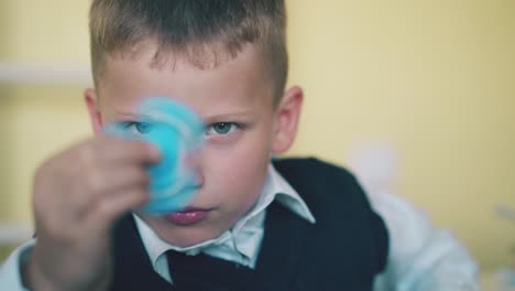 blue eyed boy holds spinner resting in light classroom