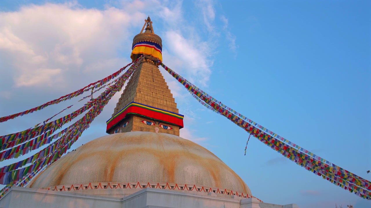 Staattinen alaviistokuva ikonista Boudhanathin stupaa ja värikkäitä rukouslippuja esitellen lämpimän auringonlaskun taivaan alla kevyiden pilvien kera Kathmandussa, Nepalissa