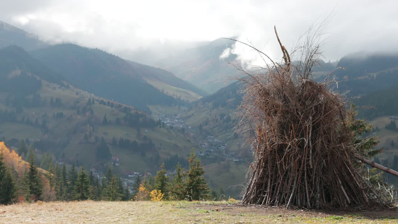 Amfiteatrul Transilvania, Moieciu de Sus, Brașov County, Romania - A Bundle of Branches Stands on a Hillside Overlooking a Misty Mountain Valley - Medium Shot