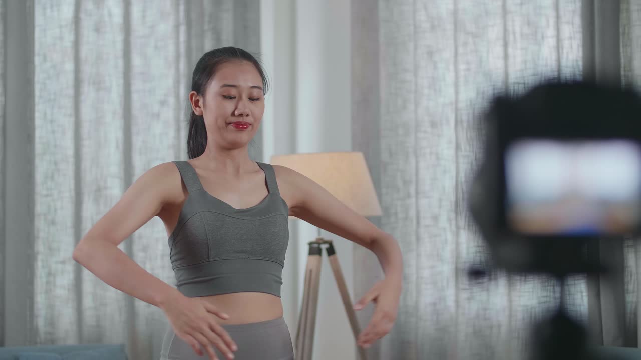 스포츠 옷을 입은 젊은 아시아 트레이너 여성이 카메라에 대화하고 집에서 가르치는 운동을 녹음하는 동안 스트레칭합니다.