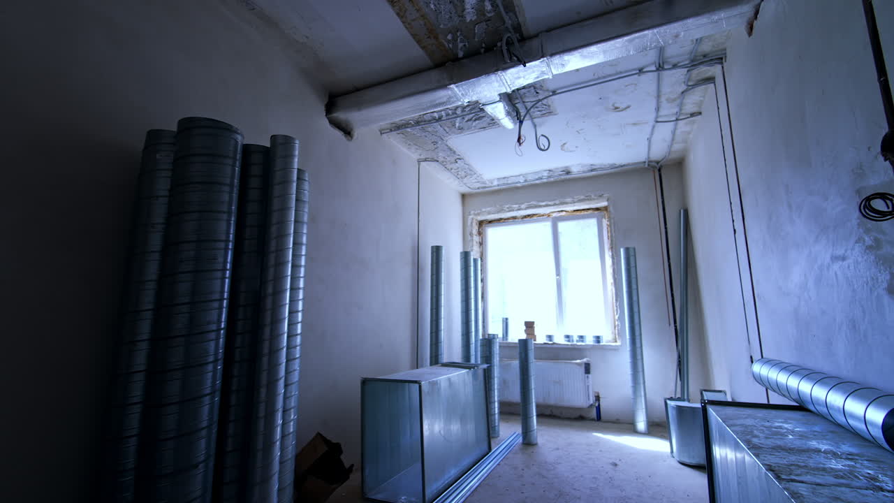 Ductwork install at construction site. A room under construction showcases metal ductwork and exposed walls with a large window letting in natural light