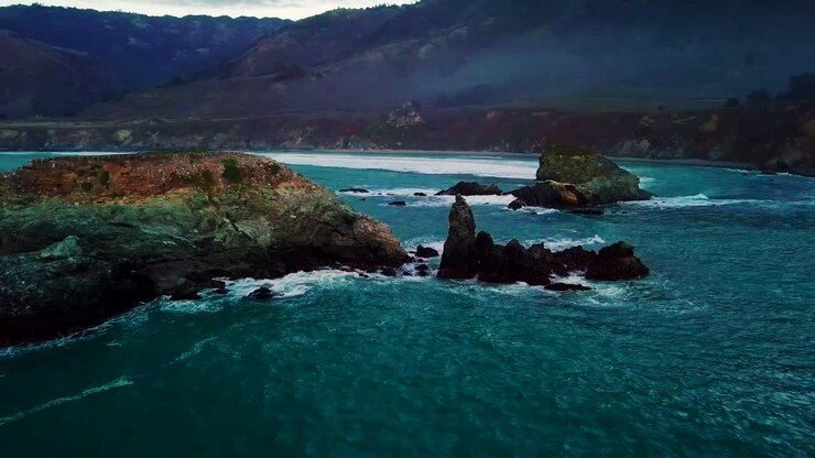 Volando vicino alle onde che si infrangono sulle rocce oceaniche a Sand Dollar Beach a Big Sur, California, al crepuscolo.