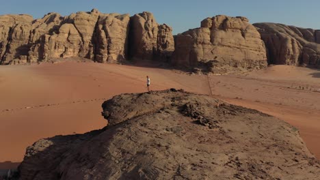 Climber's-vantage-point-over-Wadi-Rum-landscape-on-top-of-rock,-drone-arc-shot