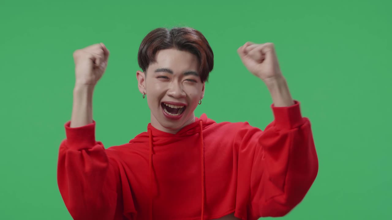 Cheerful Young Asian Transgender Male Celebrating While Standing On Green Screen In The Studio