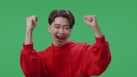 cheerful young asian transgender male celebrating while standing on green screen in the studio