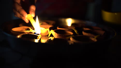 a hand lighting multiple diyas with a candle fire on occasion of diwali, the indian festival of light