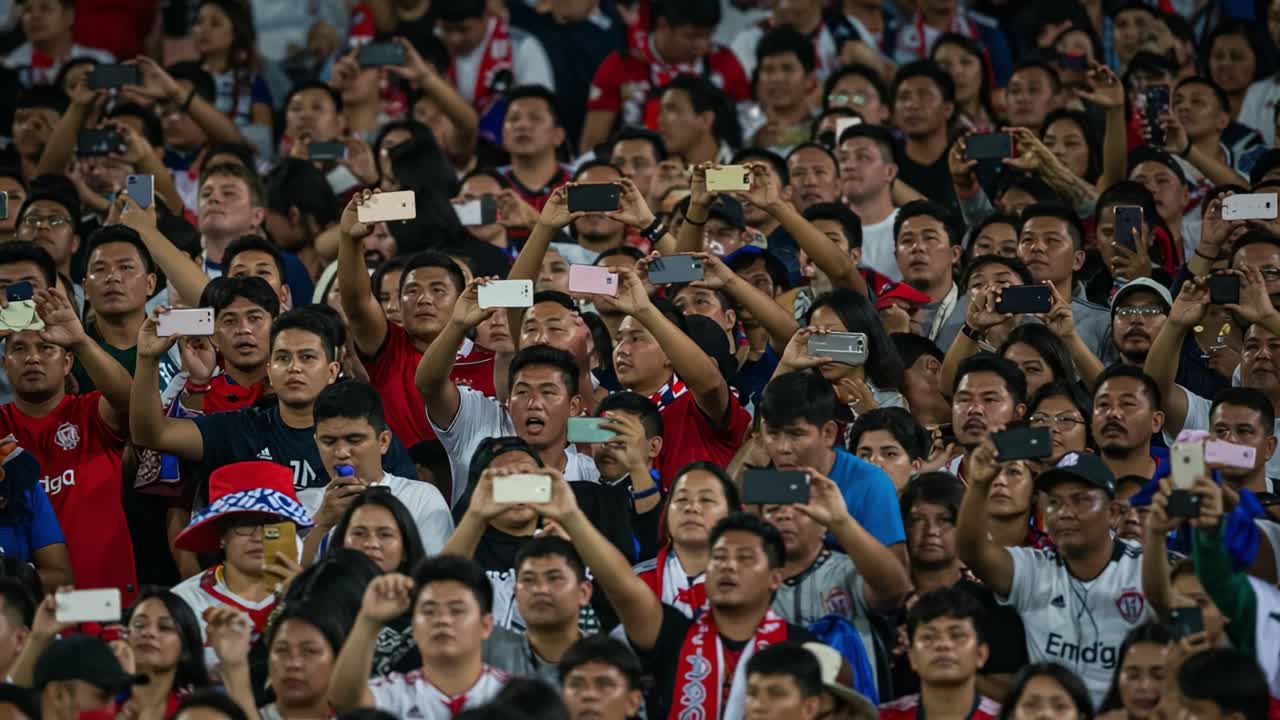 Excited Fans Capturing Moments at a Thrilling Event, Raising Phones for Photos and Videos in a Packed Stadium Atmosphere filled with Passionate Energy and Support