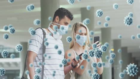 animation of virus cells over aucasian couple wearing face masks using smartphones