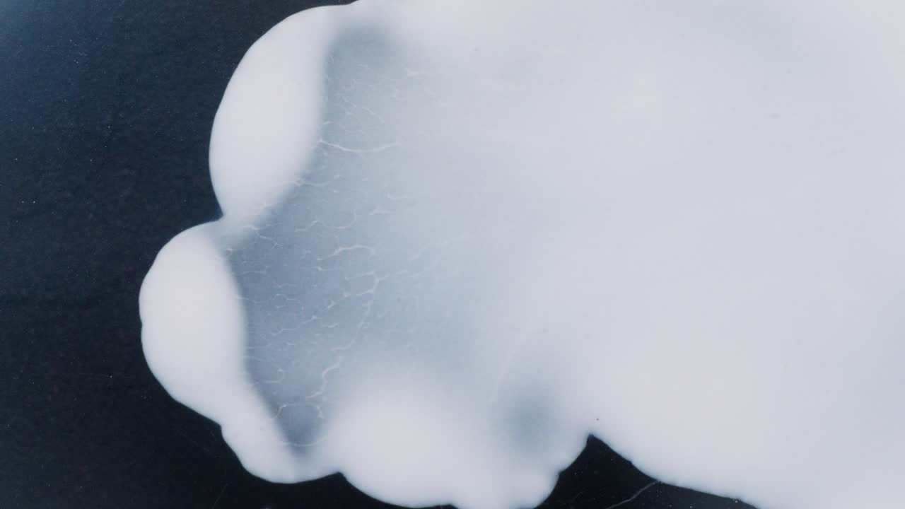White alcoholic ink slowly spreads over dark surface in abstract macro view
