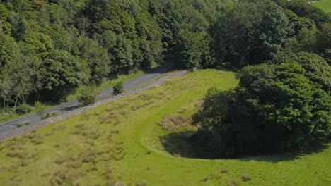 Beautiful-drone-movement-from-the-bottom-of-a-tree-covered-limestone-crag,-ascending-and-panning-revealing-valleys,-hills,-farmland,-fields,-dry-stone-walls-and-the-rural-Yorkshire-landscape